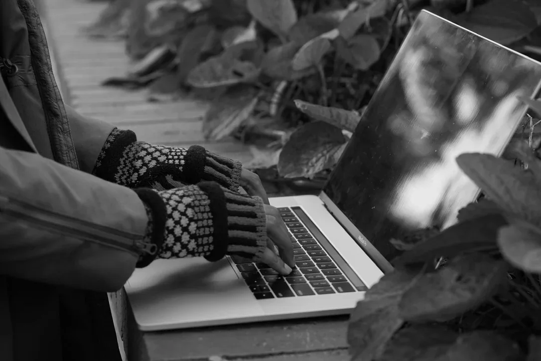 Fingerless gloves at a laptop — monochrome campaign photograph.