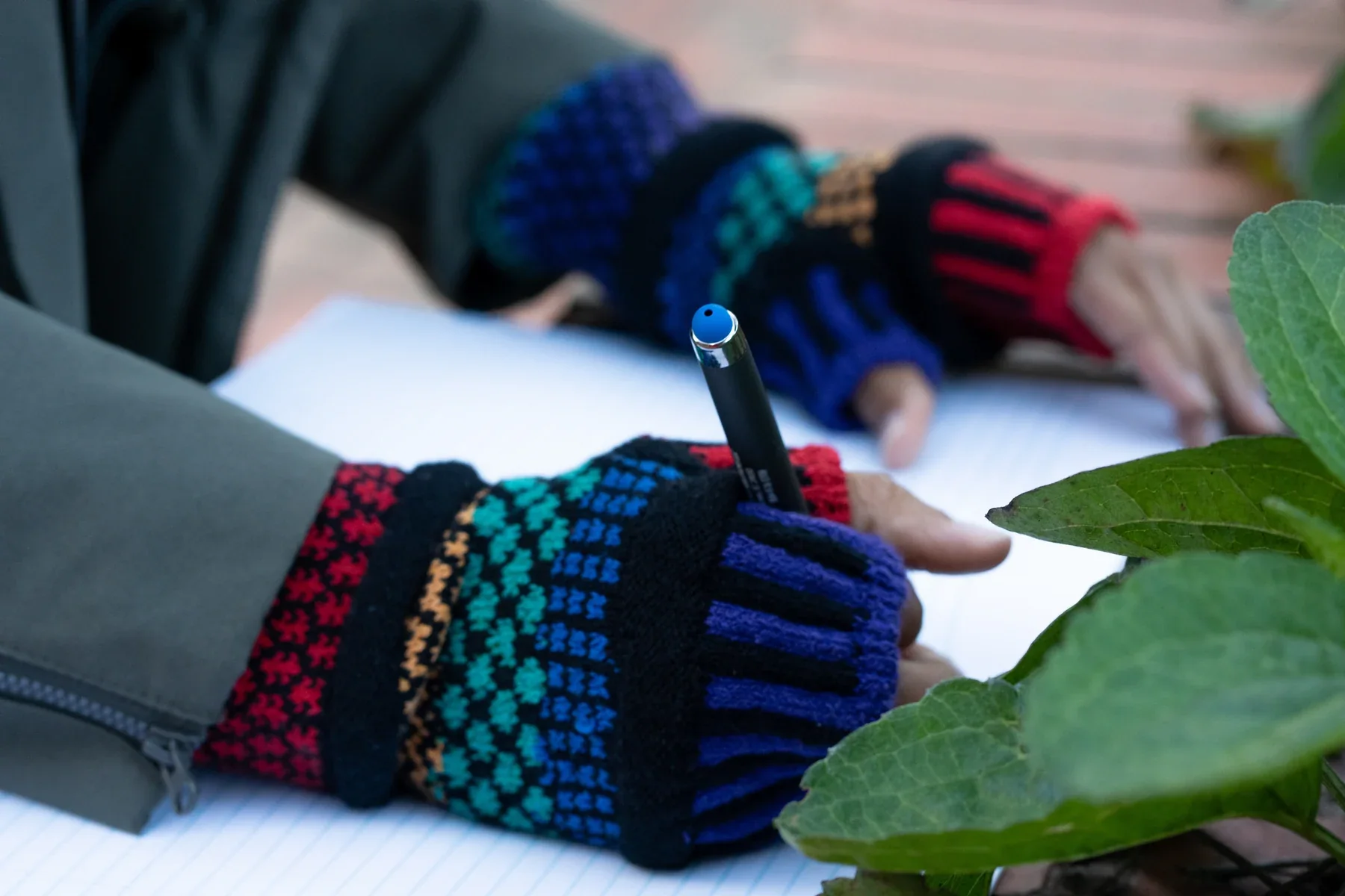 Colorful fingerless gloves in use while writing in a notebook outdoors.